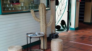 Una habitación con un rascador para gatos, dos otomanas de mimbre, una mesita con revistas y suelo de baldosas.