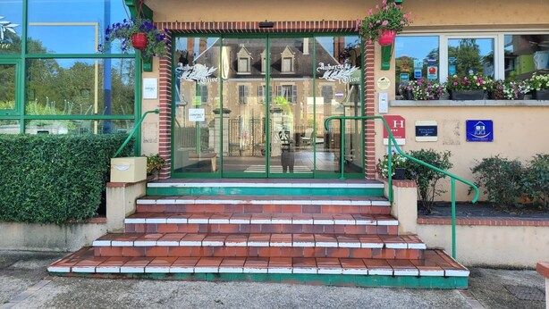 Un edificio con fachada verde, entrada de vidrio y escalones que conducen a la puerta.