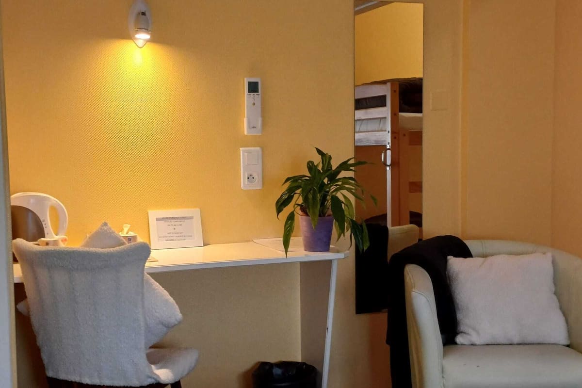 A room with a desk, chair, potted plant, and a couch.
