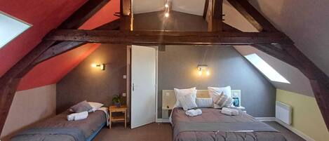 A loft-style bedroom with two beds, wooden beams, and skylights.
