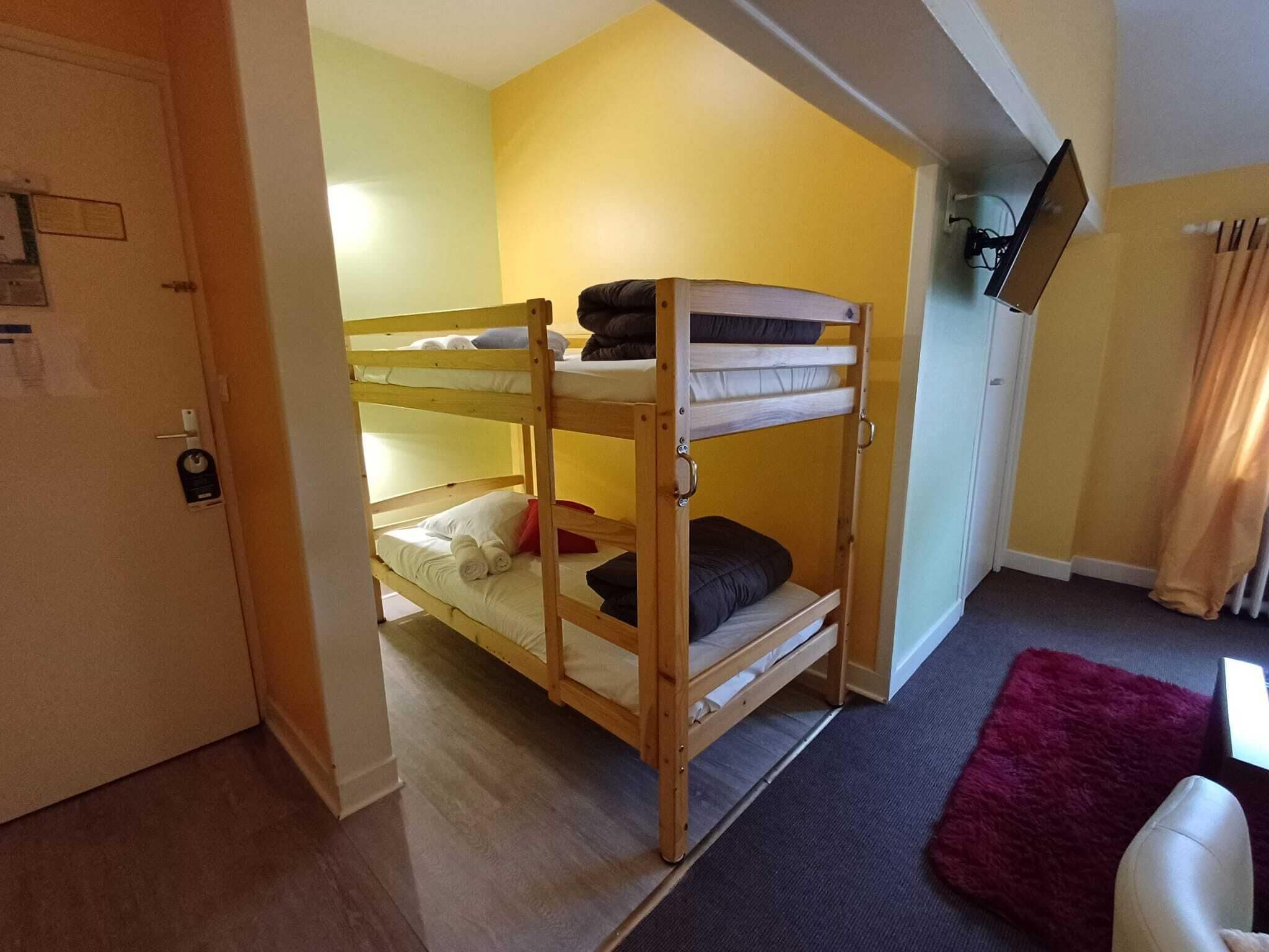 A bunk bed room with a television on the wall, a door with a lock, and a red rug on the floor.