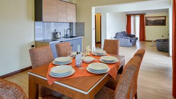 A dining area with a table set for four, surrounded by wicker chairs. A kitchen with granite countertops and wooden cabinets is visible in the background.