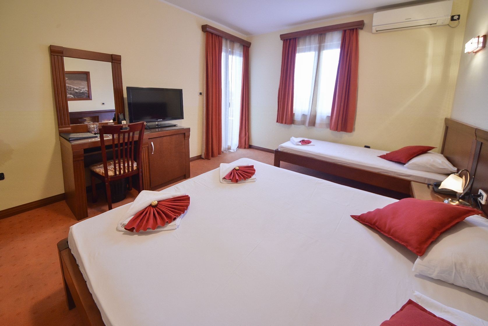 Una habitación de hotel con una cama grande, un escritorio con computadora, una silla y dos camas individuales.