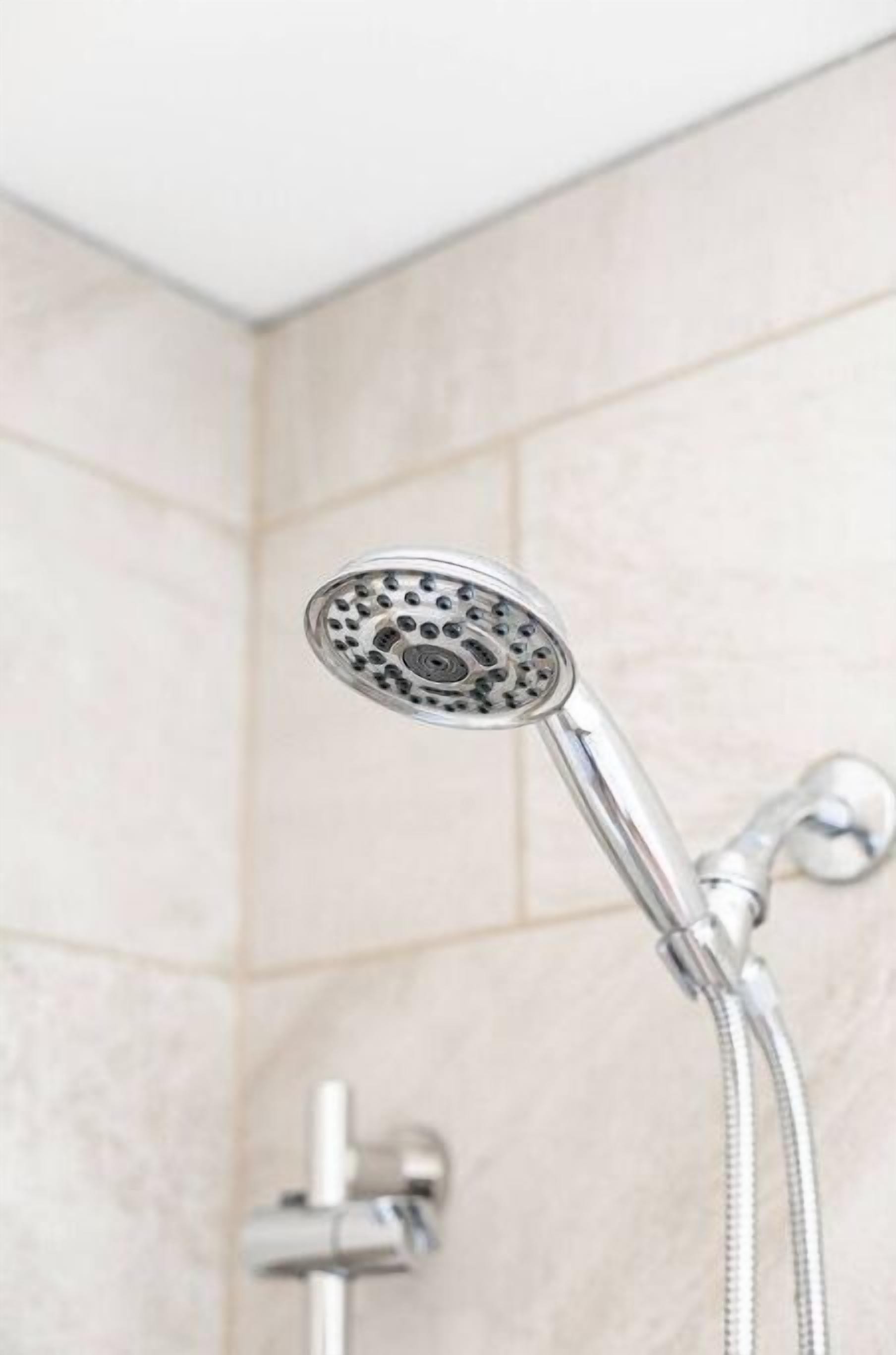 A showerhead with a handheld shower attachment in a bathroom with tiled walls.