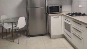 Une cuisine compacte équipée d’un réfrigérateur, d’un four à micro-ondes, d’une cuisinière, d’un four et d’une petite table à manger avec des chaises.