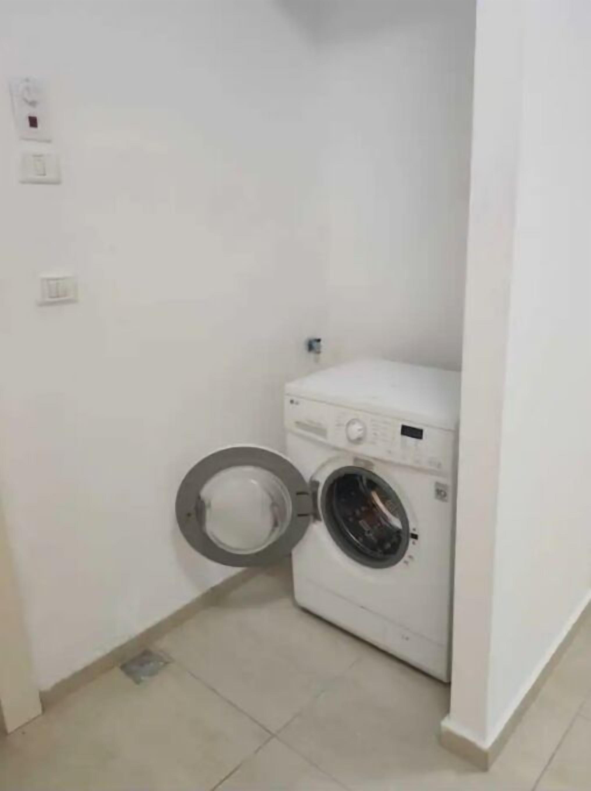 A small laundry room with a washing machine and a toilet.