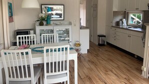 Une cuisine compacte avec des meubles blancs, une table à manger avec des chaises, un luminaire suspendu et une petite fenêtre.