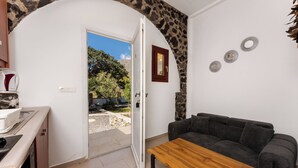 Una habitación con un arco de piedra, un sofá, una mesa de madera, una zona de cocina y una puerta que da al exterior.