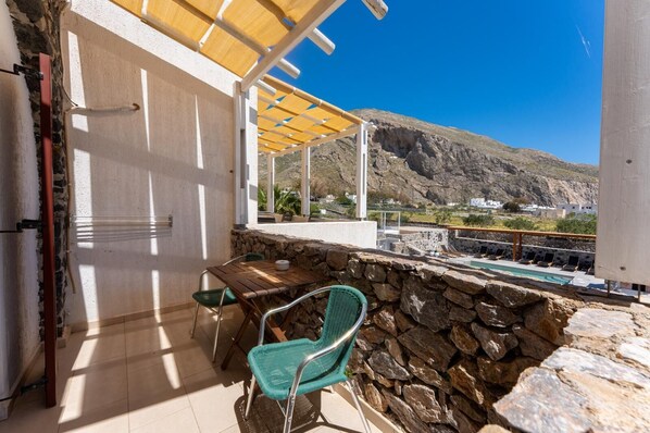 A balcony with a stone wall, a table with chairs, and a view of a mountainous landscape.