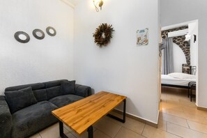 A room with a grey sofa, a wooden table, a wall-mounted decorative wreath, and a bed with a stone wall backdrop.