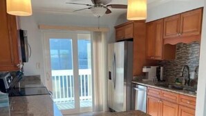 Une cuisine dotée de plans de travail en granit, de meubles en bois, d’un réfrigérateur en acier inoxydable et de deux luminaires suspendus.