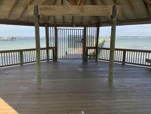 Una terraza de madera con barandilla metálica, que da vista a una masa de agua y una costa lejana.