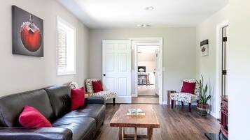 A living room with a black leather sofa, a wooden coffee table, and a door leading to a dining area.