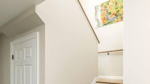 Un escalier avec des marches en bois et des murs blancs, menant à une porte.