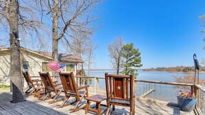 A wooden deck with rocking chairs, a flag, and a view of a lake.