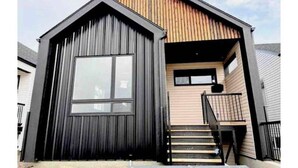 A modern house with a large garage door, a wooden upper floor, and a staircase leading to a second level. - The Northside Nest (Lethbridge)