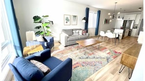 A modern living room with a sofa, coffee table, and a dining area with chairs. - The Northside Nest (Lethbridge)