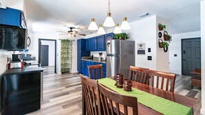 A modern kitchen with blue cabinets, a stainless steel refrigerator, and a dining area with wooden chairs and a green tablecloth. - Pool Home in Ocala -Casa Oasis (Ocala)
