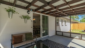 A covered patio with a glass door leading to a dining area, a bench with cushions, and potted plants on the wall. - Pool Home in Ocala -Casa Oasis (Ocala)