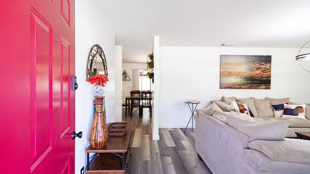 A modern living room with a beige sofa, a dining area with a table and chairs, and a vibrant red door. - Pool Home in Ocala -Casa Oasis (Ocala)