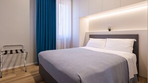 Une chambre d’hôtel moderne avec un lit bien fait, une table de chevet et une fenêtre ornée de rideaux bleus.