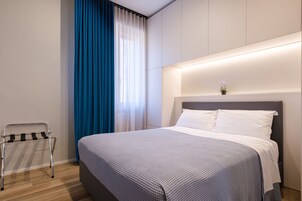 Una camera d'albergo moderna con un letto rifatto, un comodino e una finestra con tende blu.