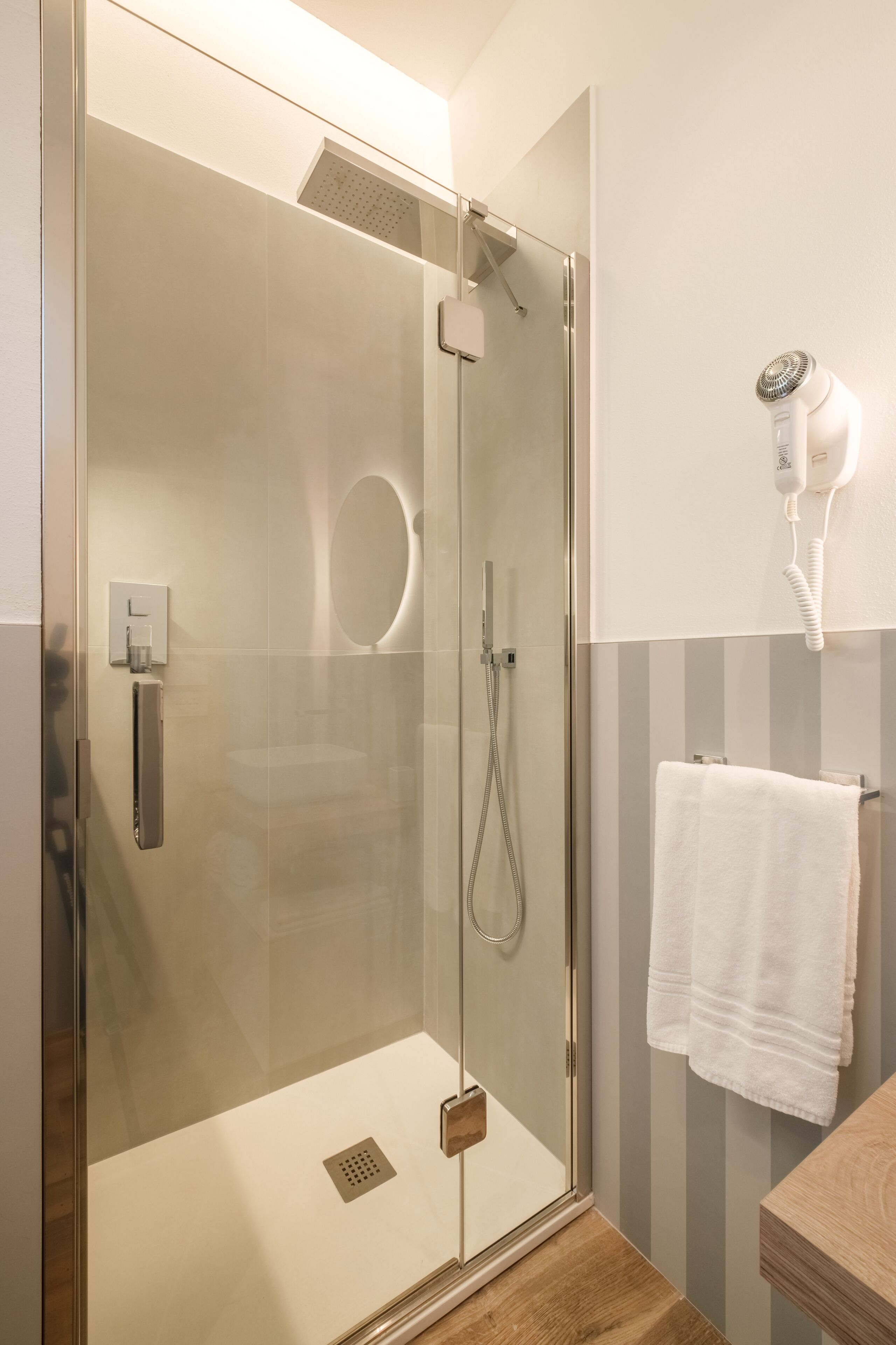 A modern bathroom with a glass-enclosed shower, a hairdryer mounted on the wall, and a towel hanging on a rack.
