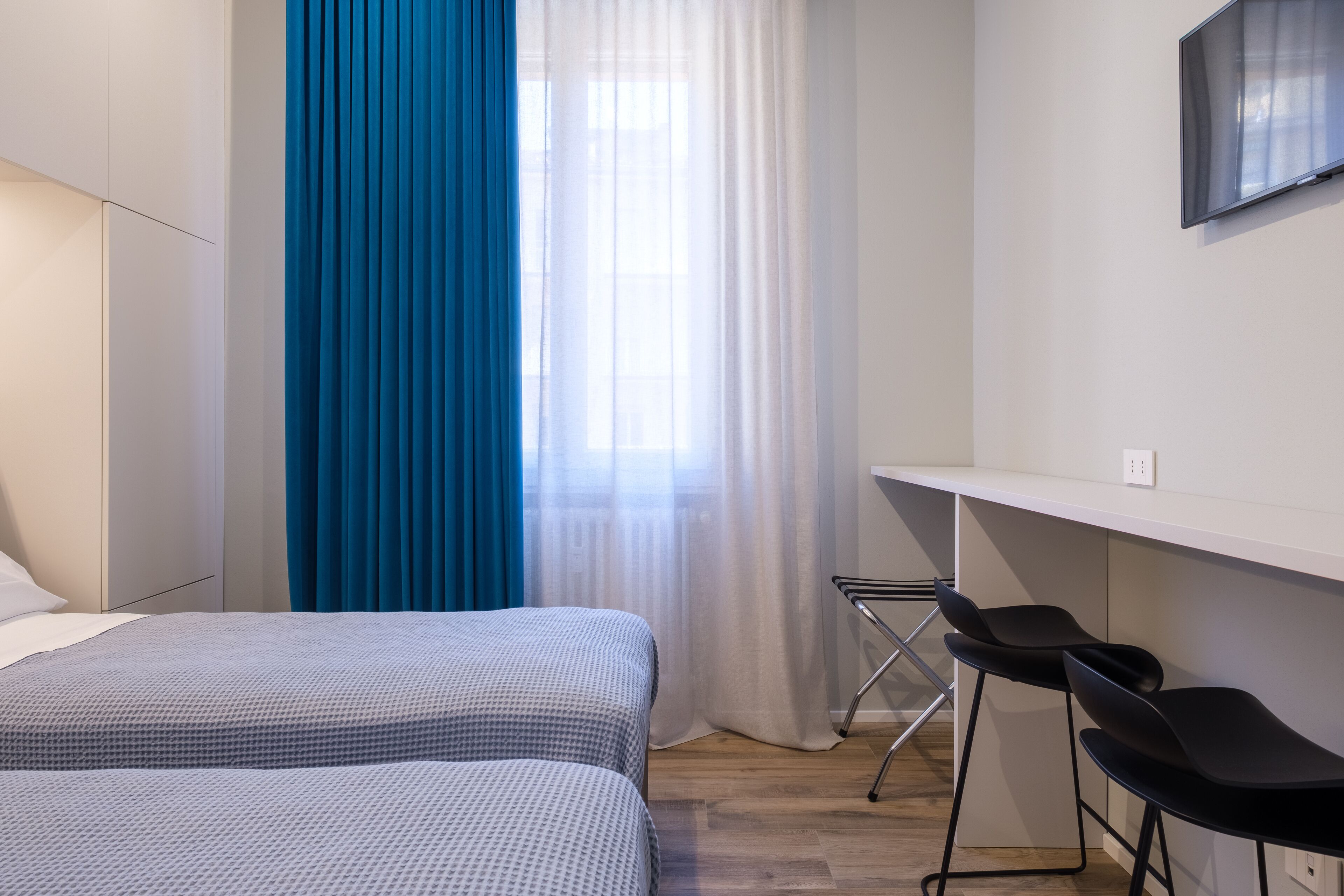 A hotel room with a bed, a desk, two chairs, and a window with curtains.