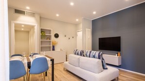 Un salon moderne comprenant un canapé, une table à manger avec des chaises, un téléviseur fixé au mur et un radiateur.