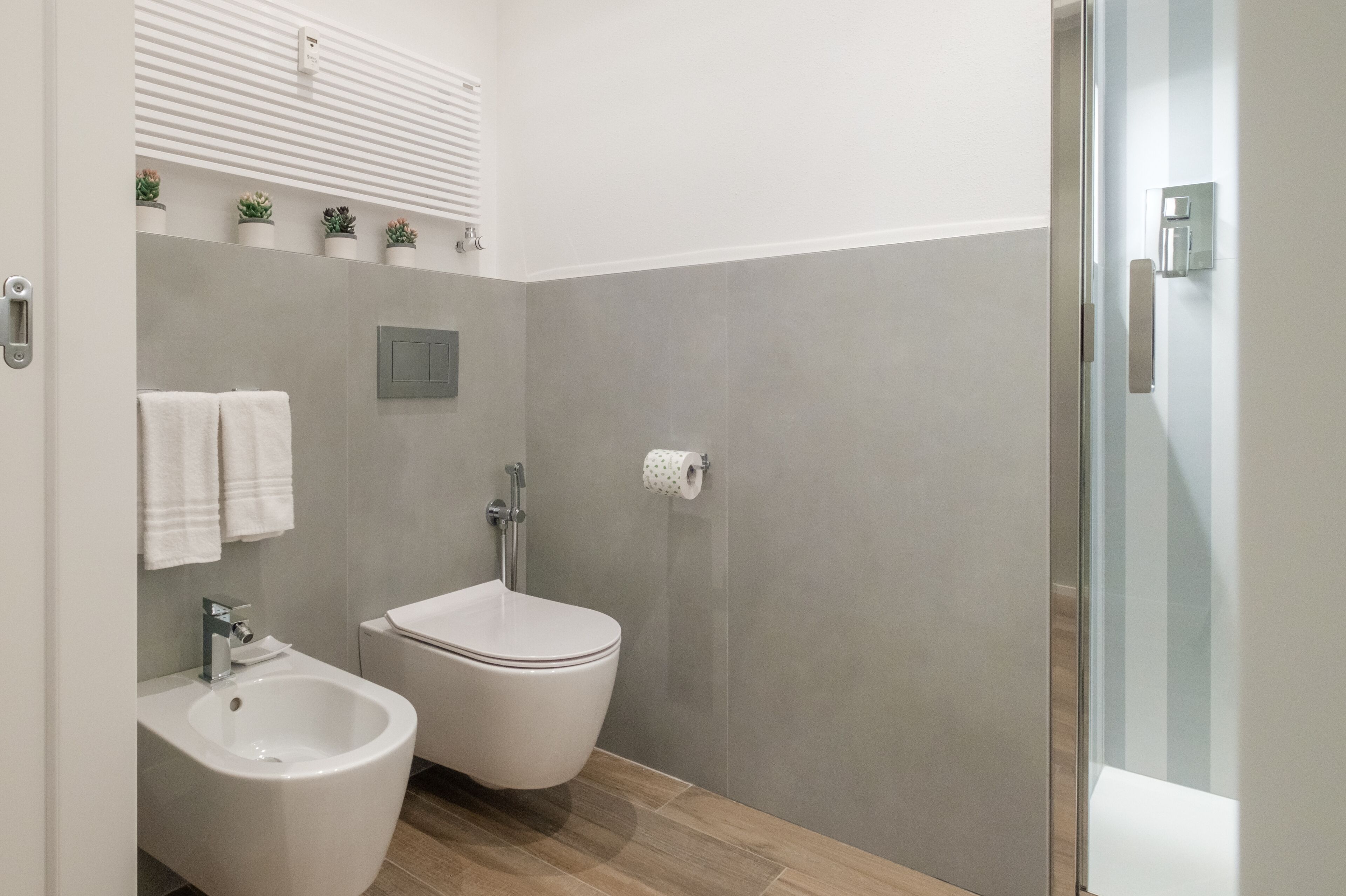 A modern bathroom with a bidet, toilet, and bidet tub. There are potted plants on the wall and a towel rack.