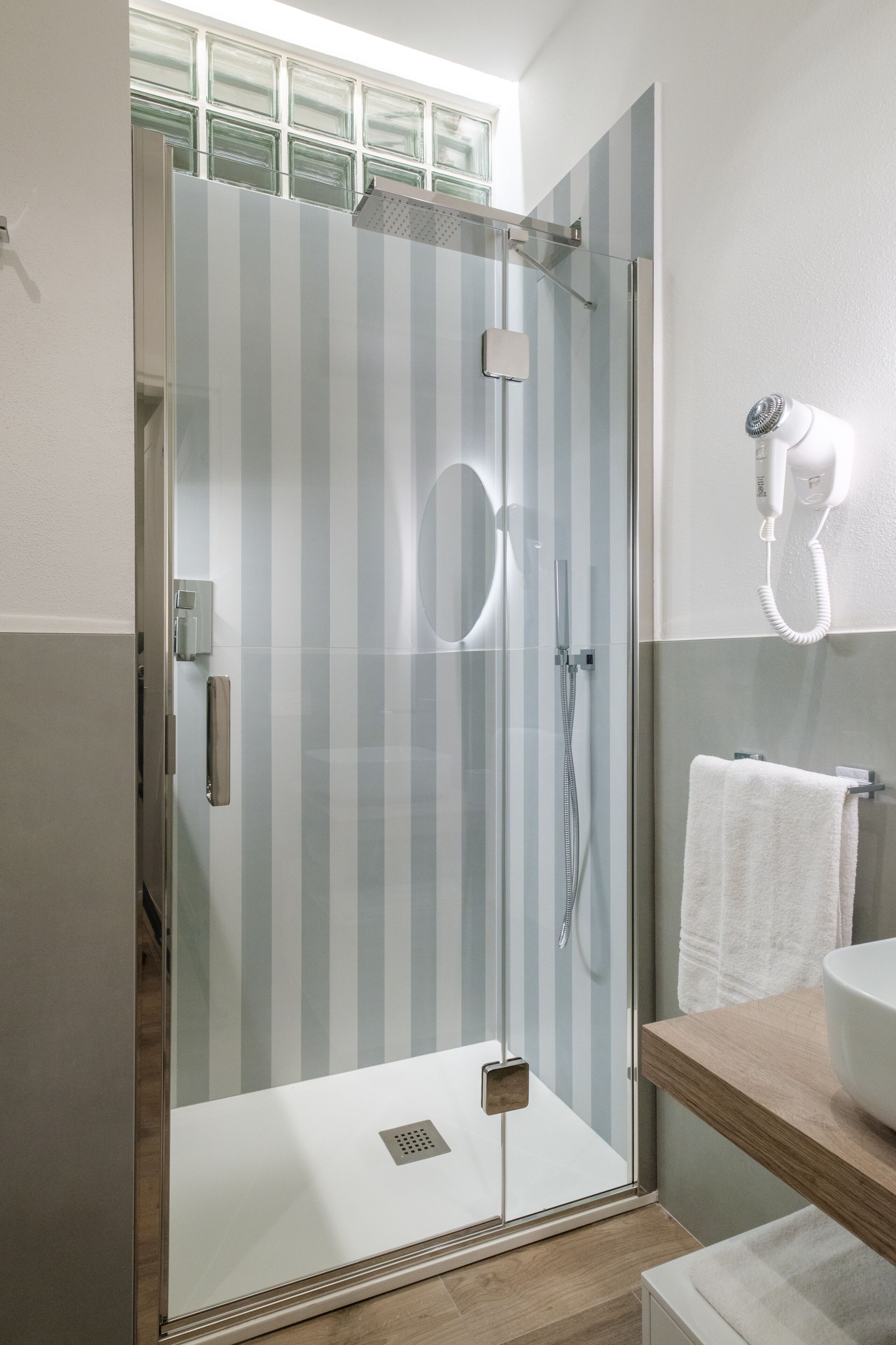 Une salle de bain moderne dotée d’une douche à parois de verre, d’un sèche-cheveux fixé au mur et d’un meuble-lavabo en bois avec un évier.