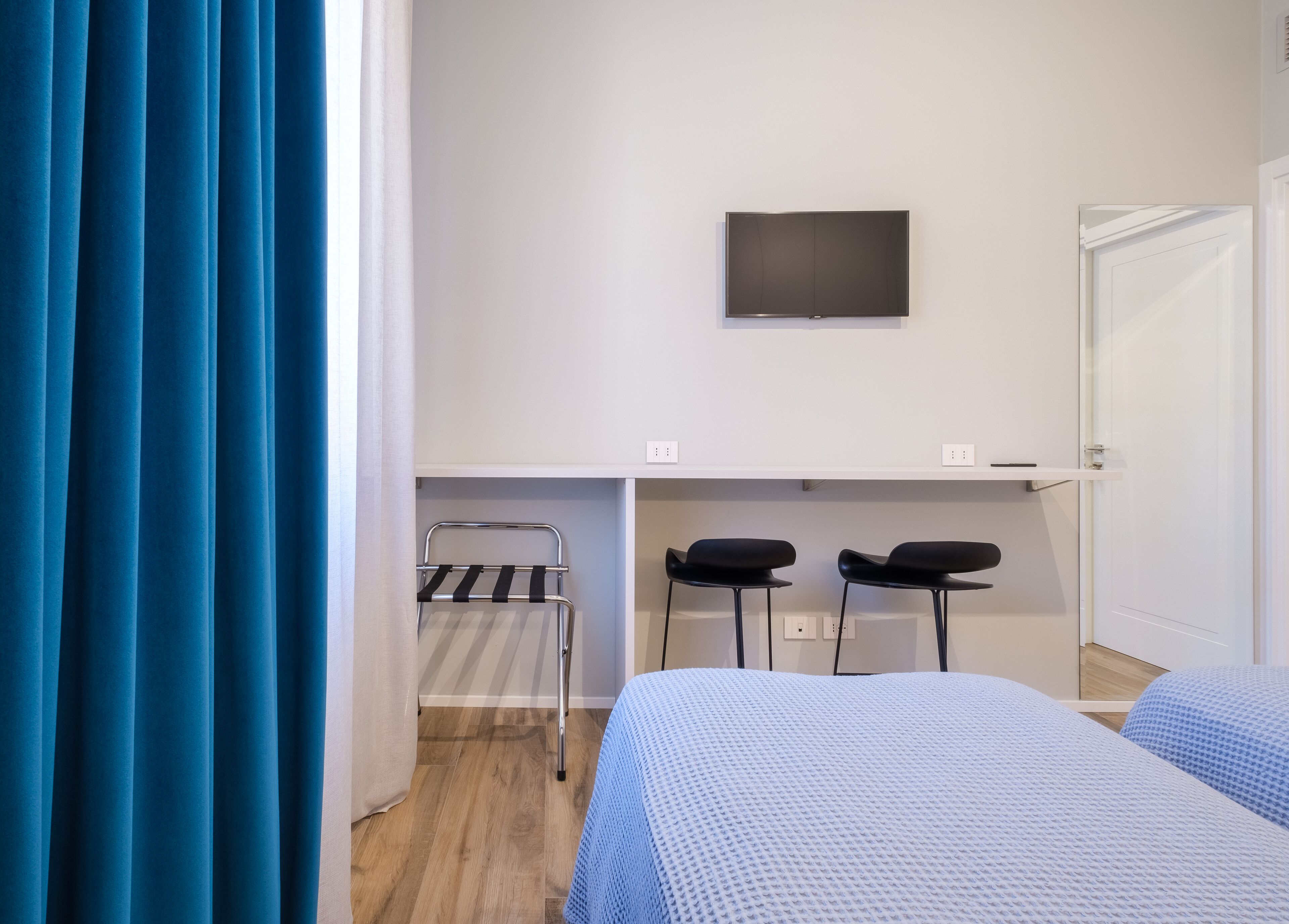 Une chambre d’hôtel avec un lit, un téléviseur fixé au mur, une petite table, deux chaises et une fenêtre avec des rideaux.