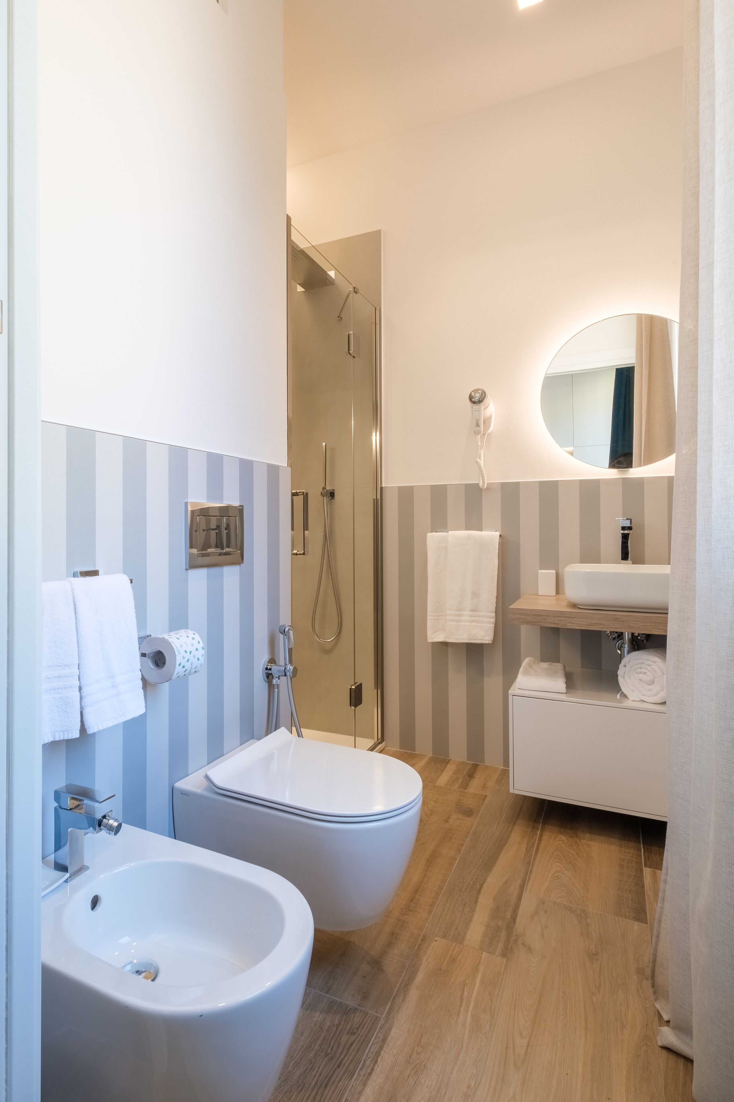 A modern bathroom with a bidet, a toilet, a sink, and a shower.