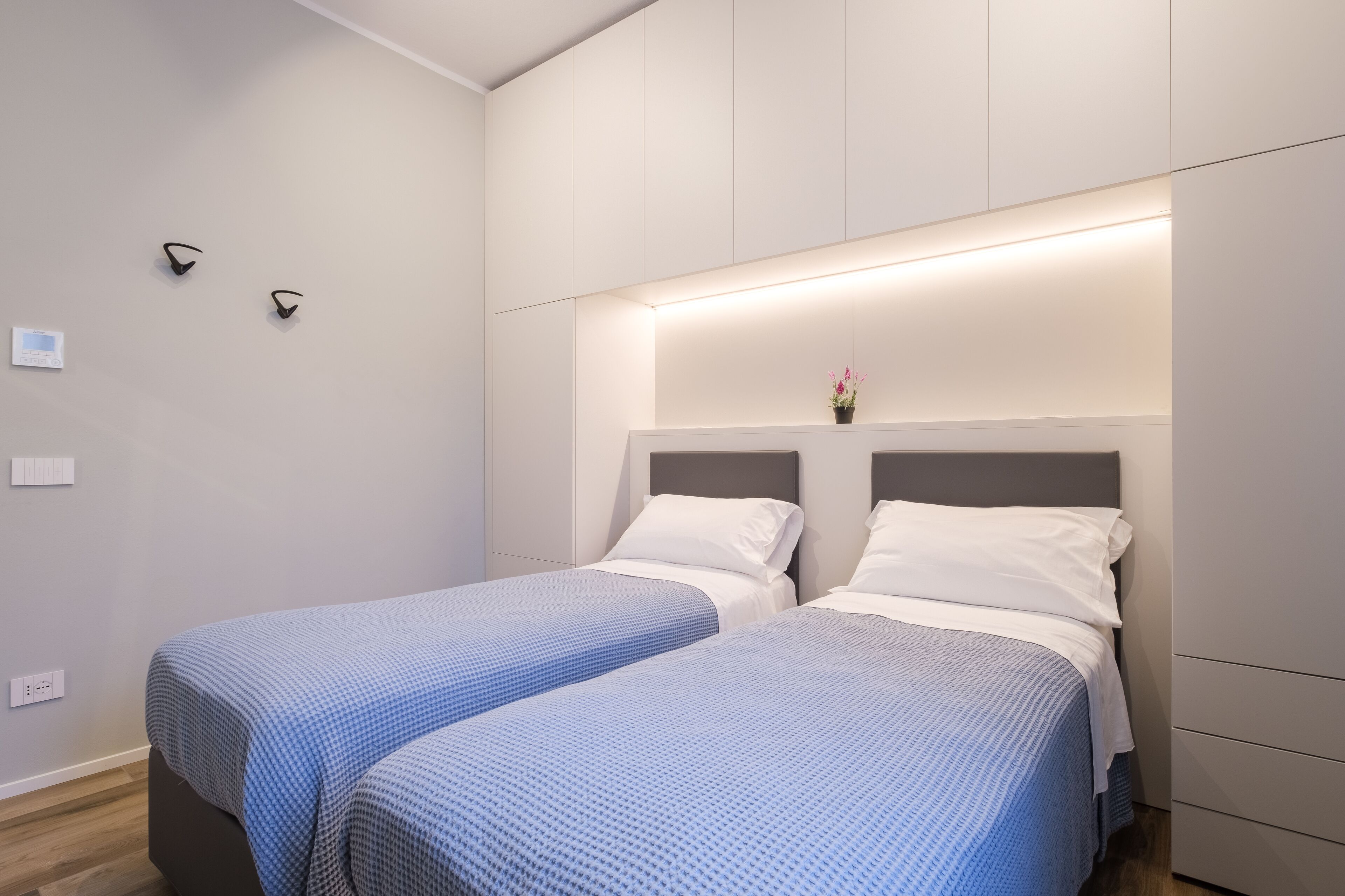 Quarto de hotel moderno com duas camas de solteiro, uma mesa de cabeceira e uma pequena planta em vaso sobre ela.
