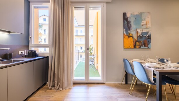 Une cuisine moderne dotée d’une porte-fenêtre coulissante donnant sur un balcon, un coin repas avec des chaises bleues et un tableau accroché au mur.