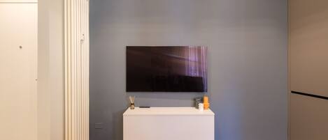 A modern room with a flat-screen TV mounted on a white console table, a radiator, and a wooden floor.