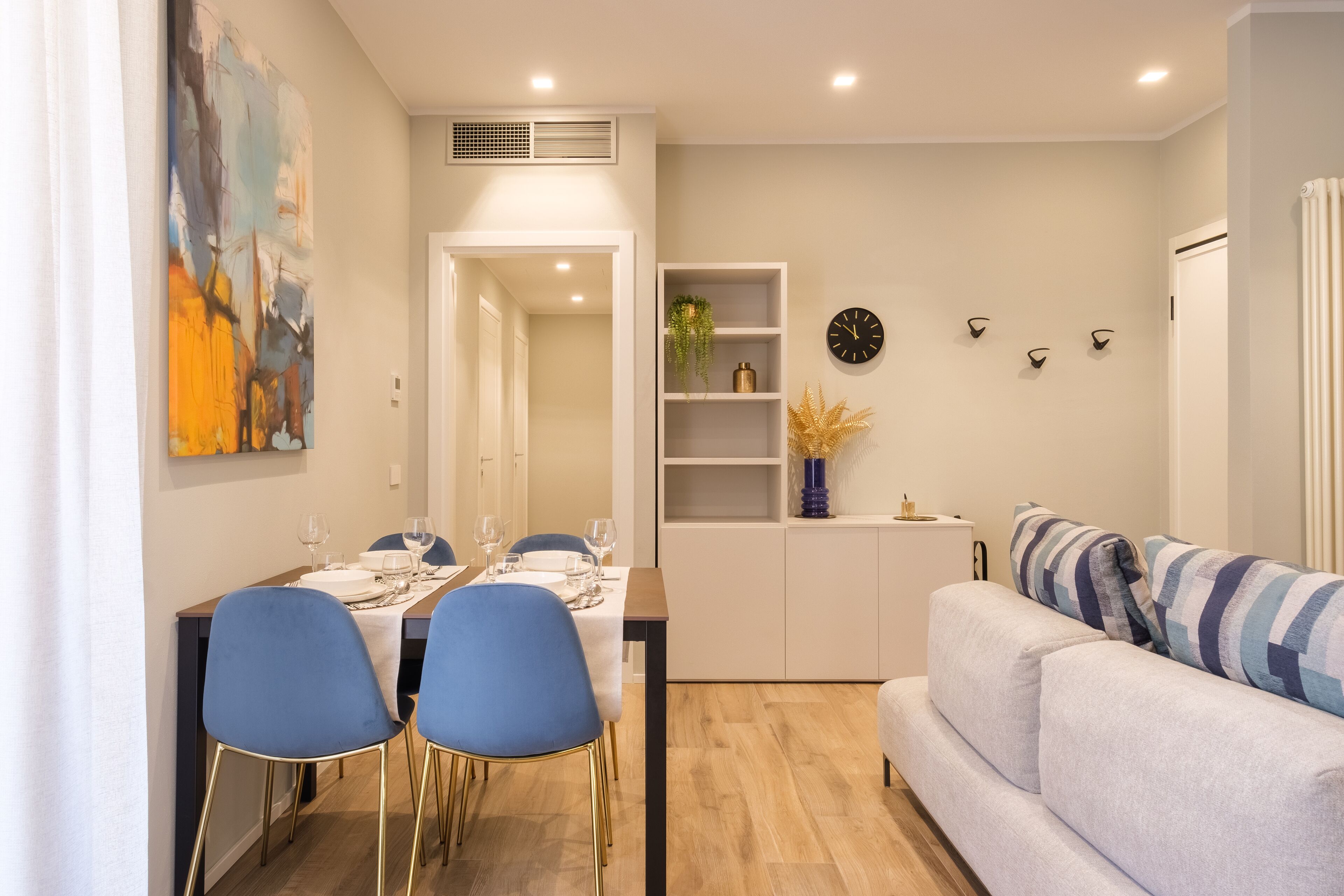 A modern living room with a sofa and a dining area with blue chairs and a table set for four.