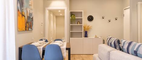 A modern living room with a sofa and a dining area with blue chairs and a table set for four.
