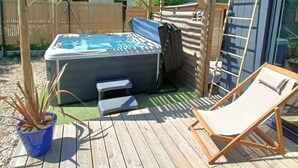 Ett trädäck med ett bubbelbad, en solstol och en pergola.
