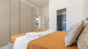 A hotel room with a bed, a wardrobe, a bathroom with a shower, and a door leading to another room.