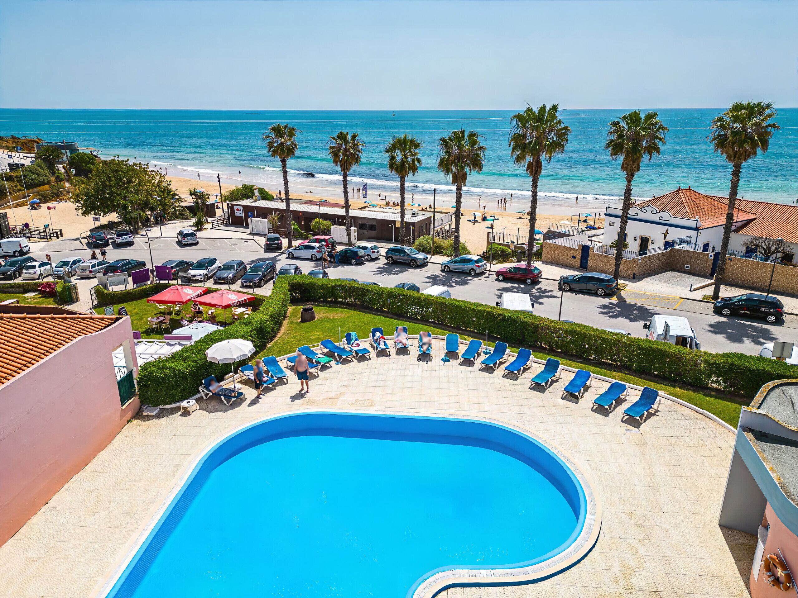 A pool area with lounge chairs, a swimming pool, and a view of the beach and ocean.