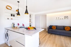 A modern kitchen with a central island, pendant lights, and a dining area with a sofa and cushions.