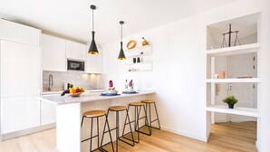 A modern kitchen with white cabinetry, a marble countertop, and a central island with stools. - Apartment w/ Pool in Praia do Vau (Portimão)