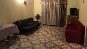 A living room with a sofa, a red chair, a television on a wooden cabinet, a fan, and a table with a checkered tablecloth. - B&B rent rooms  (Chaguanas)