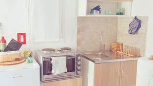Eine kleine Küche mit Herd, Backofen und Spüle. Es gibt Schränke, eine Arbeitsplatte und ein Fenster mit Jalousie.