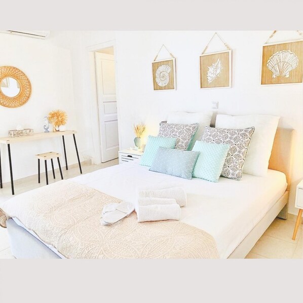 A modern bedroom with a large bed, multiple pillows, a bedside table, a mirror, and wall art.