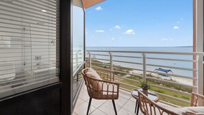 Un balcon avec vue sur la mer, une chaise, une petite table et une plante en pot.
