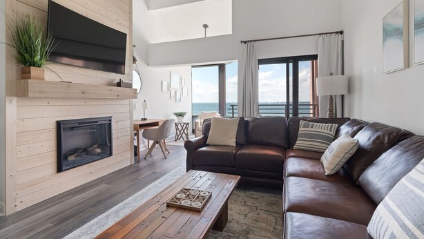 Un salon moderne avec une cheminée, un canapé en cuir, une table basse en bois et une vue sur la mer.