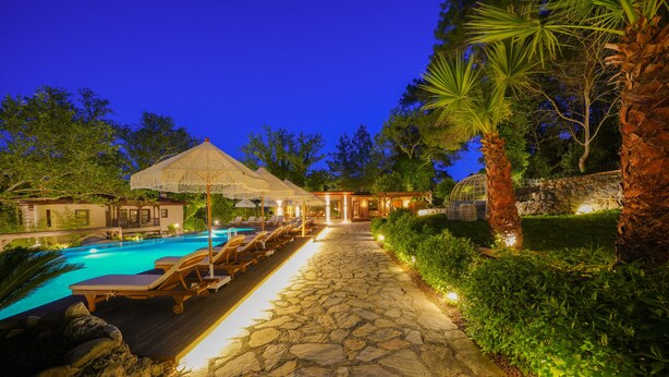 A stone pathway leading to a pool area with lounge chairs and a covered seating area. - Nuup Hotel (Marmaris)