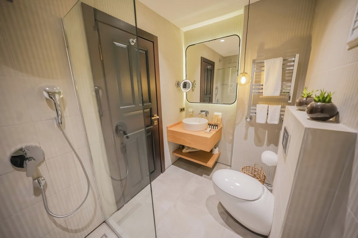 Un baño moderno con ducha envuelta en vidrio, tocador de madera con lavamanos, inodoro y un espejo grande.